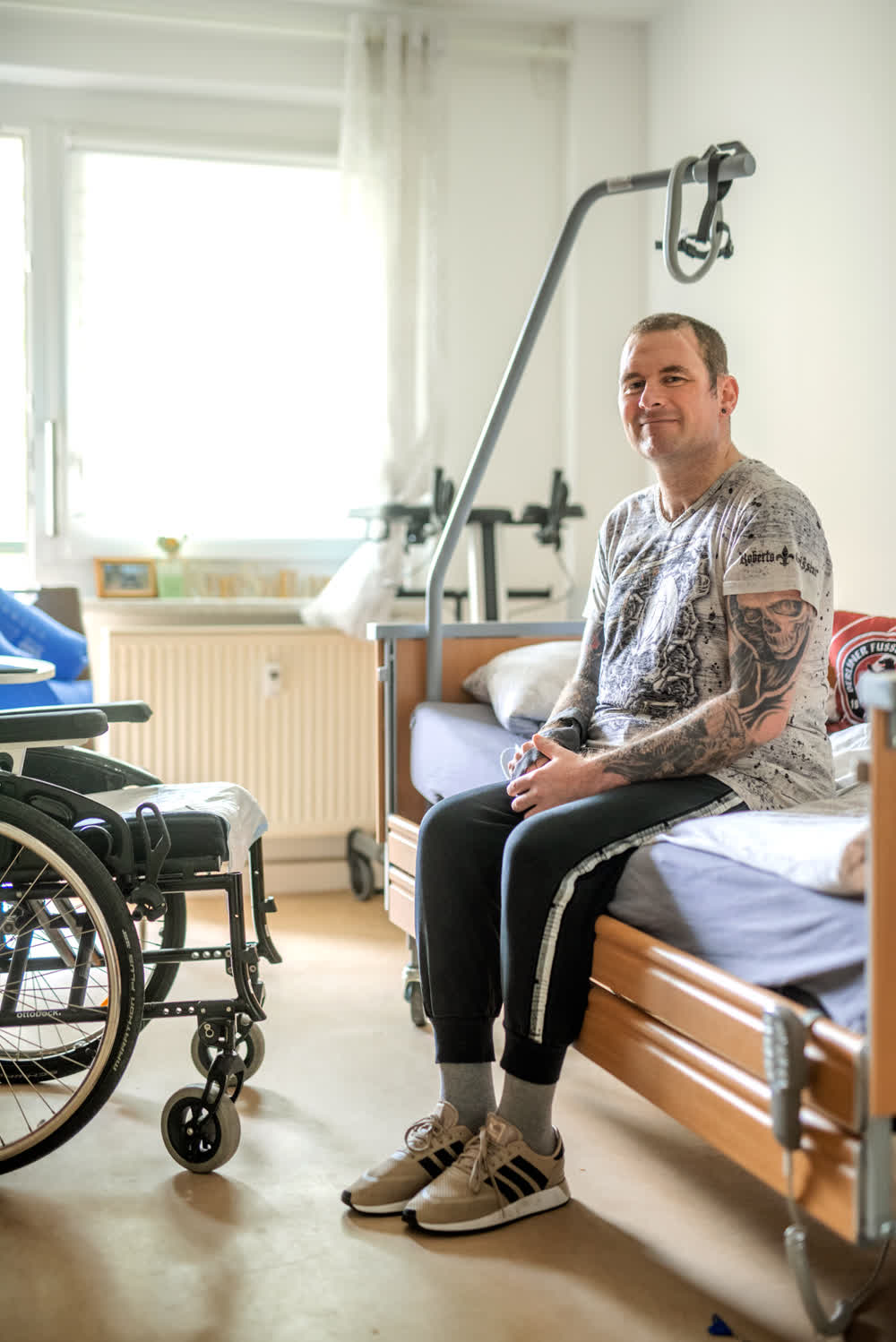mann-im-zimmer-auf-bett-sitzend-mit-rollstuhl